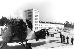 Ein Bild von 1936, dem Eröffnungsjahr des Flughafens Rhein-Main. Flugzeug vor dem Empfangsgebäude mit Menschen und weiteren Flugzeugen im Vordergrund.